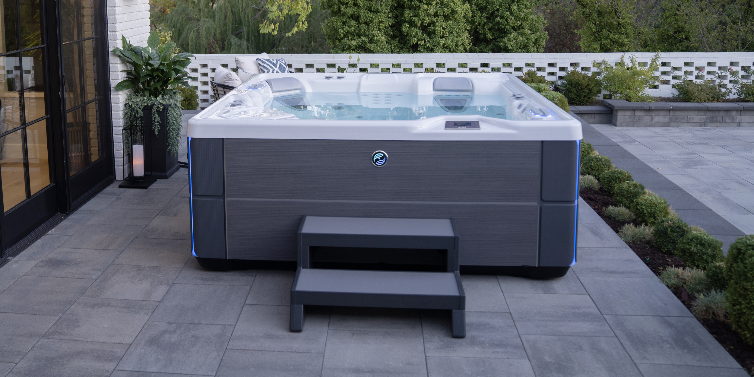 A portable hot tub with its cover open on a stone patio overlooking a lake